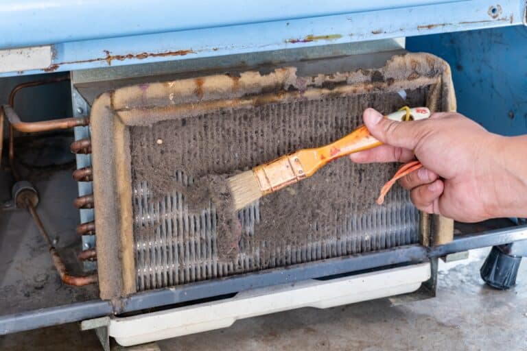A man's hands held a brush to clean the dirty condensing unit.